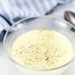 Keto white sauce in a glass bowl topped with cracked black pepper, with a striped napkin and spoon