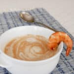 Low carb shrimp bisque in a white bowl with a swirl of cream and a pan-fried shrimp on the rim