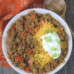 Low carb chili in a white bowl topped with shredded cheddar, sour cream and sliced green onions