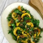 Delicata squash with kale and pecans in an oval serving dish with wooden spoons