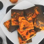 Keto Halloween brownies with an orange cheesecake swirl stacked on a white plate with orange ornaments