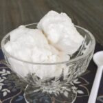 Two scoops of sugar free no carb ice cream in a glass dessert bowl with a white spoon