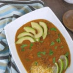 Low carb taco soup in a white bowl garnished with avocado, fresh cilantro, shredded cheese and lime wedges