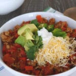 Low carb turkey chili in a white bowl topped with avocado, sour cream, jalapeno, cilantro and cheese