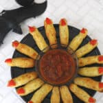Low carb witch fingers with red pepper nails arranged in a circle around a bowl of salsa