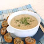 Creamy cauliflower fennel soup in a white bowl garnished with fennel fronds, with garlic crostini