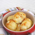 Keto pão de queijo rolls piled in a small red dish on a striped napkin