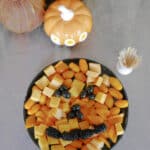 Keto Halloween snack tray shaped like a jack-o'-lantern, with cheddar cubes, orange tomatoes and cantaloupe and an olive and blackberry face