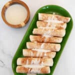 Low carb tortilla cinnamon roll-ups on a green platter with a bowl of cream cheese glaze
