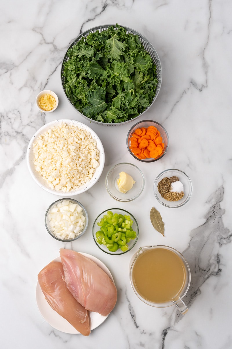 Ingredients for chicken kale soup: raw chicken breasts, kale, cauliflower rice, carrot, celery, onion, broth and seasonings
