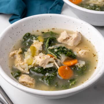 Square close-up of a bowl of chicken kale soup with chicken, kale and carrots