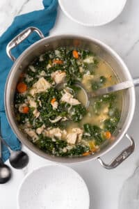 Chicken kale soup simmering in a large stainless steel pot with a ladle