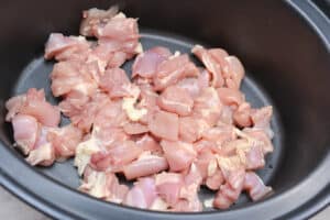 Raw chicken thigh pieces in the bottom of a slow cooker