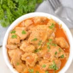 Keto slow cooker butter chicken in a white bowl with fresh parsley and a fork