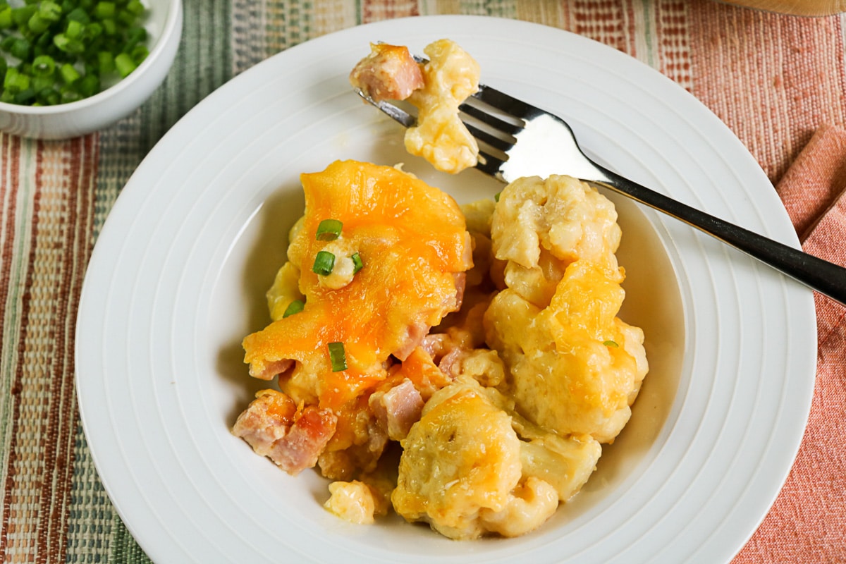 A serving of cheesy ham cauliflower casserole on a white plate with a fork