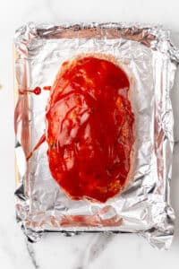 Unbaked turkey meatloaf topped with sugar free ketchup on a foil-lined baking sheet