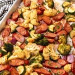 Keto sheet pan sausage with roasted broccoli, cauliflower, zucchini and red onion on a baking sheet