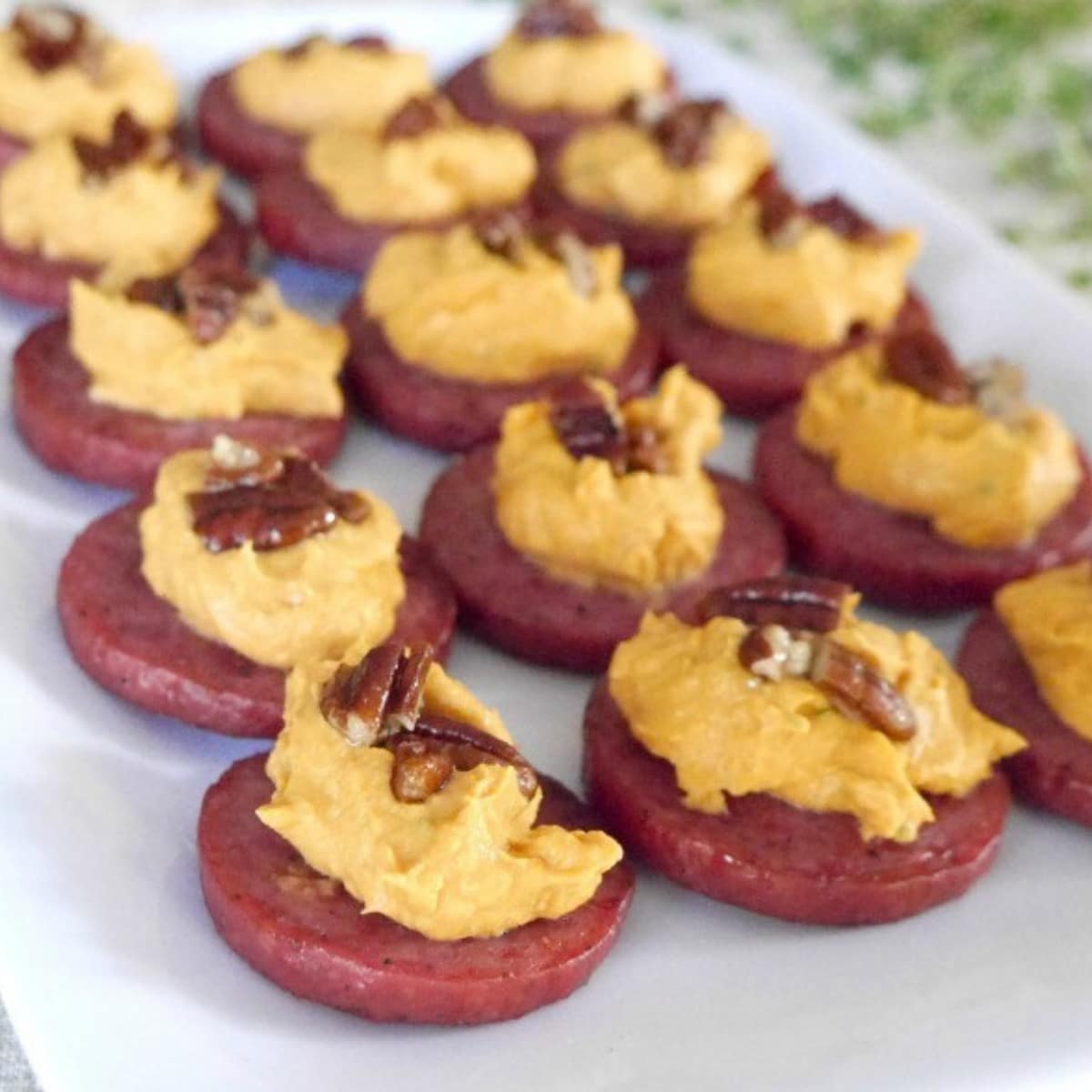 Baked sausage and pumpkin bites topped with caramelized pecans on a white platter