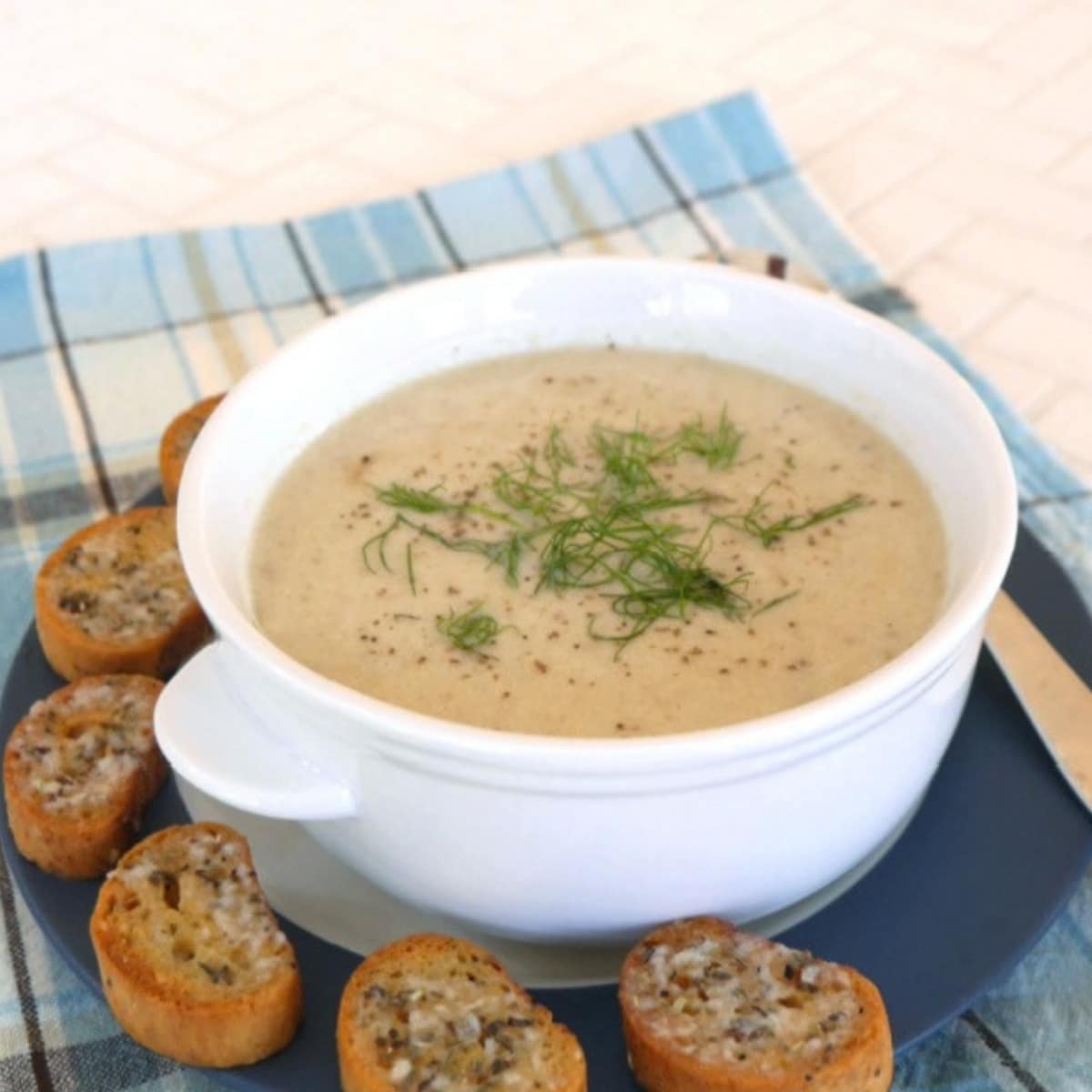 Creamy cauliflower fennel soup in a white bowl with fennel fronds and garlic crostini