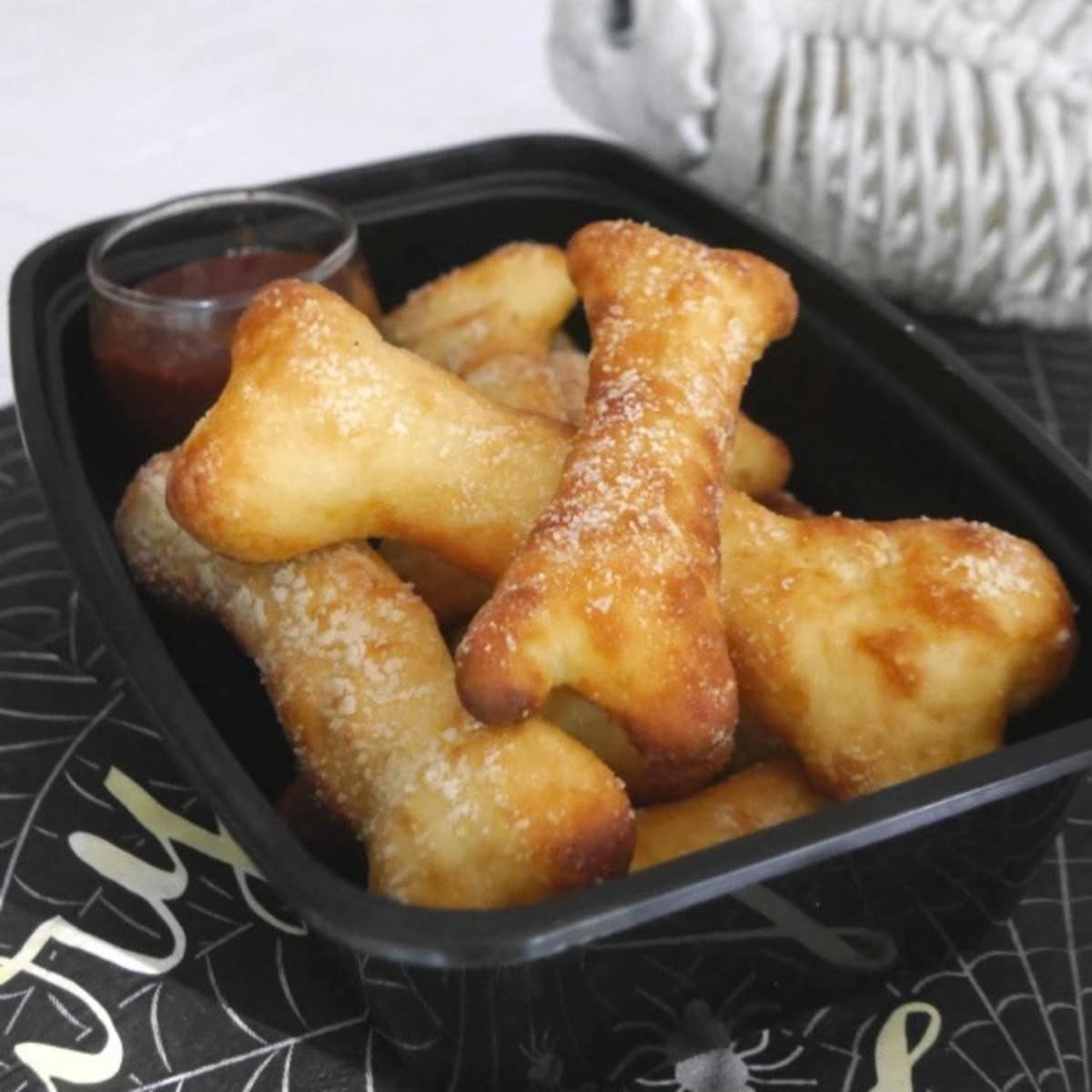 Fathead breadstick bones sprinkled with Parmesan in a black tray with a small jar of dipping sauce