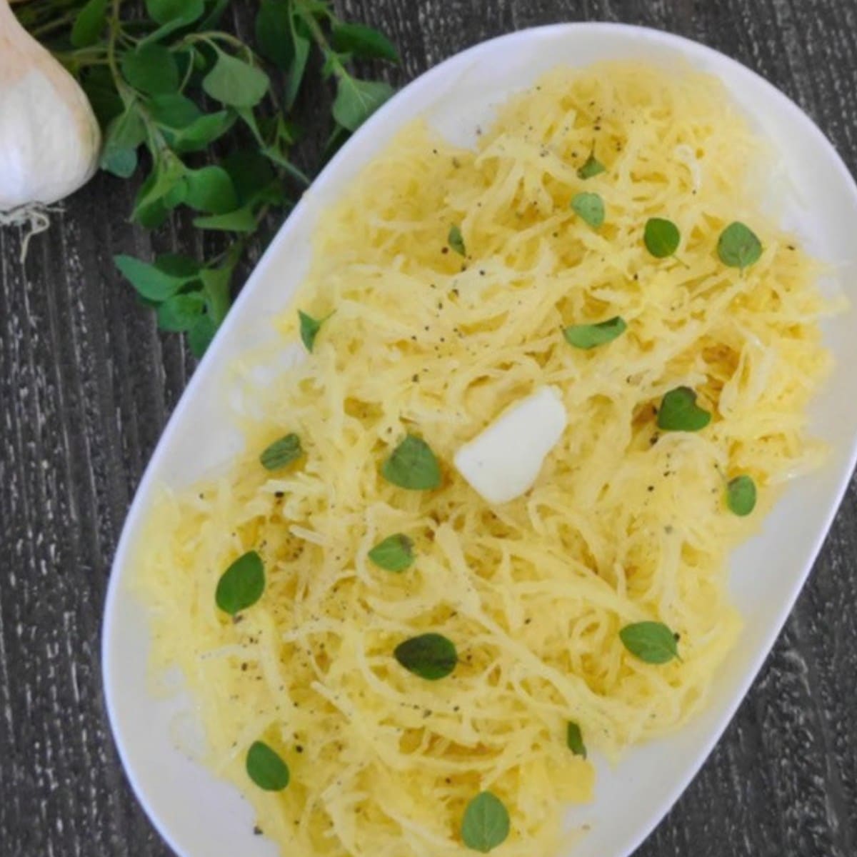 Garlic butter spaghetti squash with Parmesan and fresh oregano on a white platter
