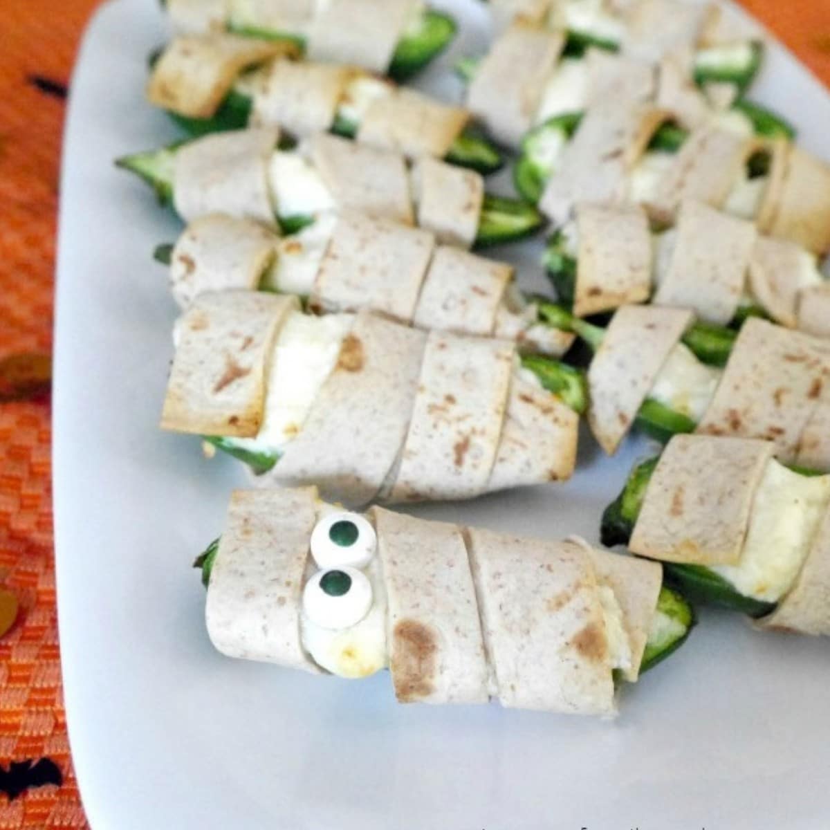 Mummy-wrapped Halloween jalapeño poppers with candy eyes on a white platter