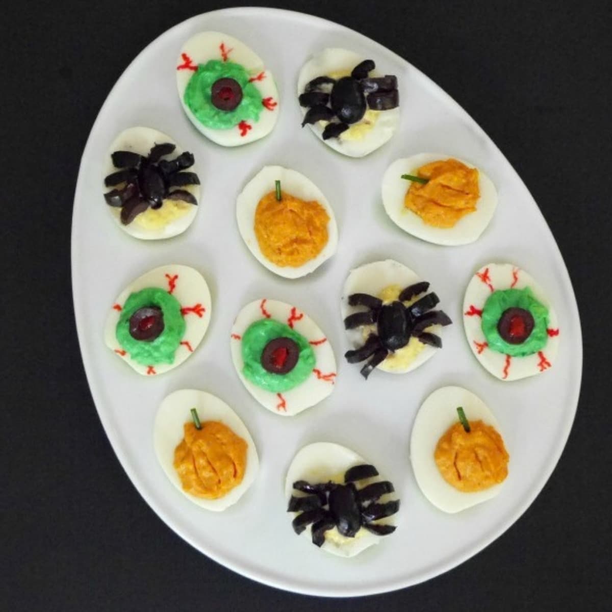 Halloween spider deviled eggs with olive spiders, pumpkin and zombie eye deviled eggs on a white platter
