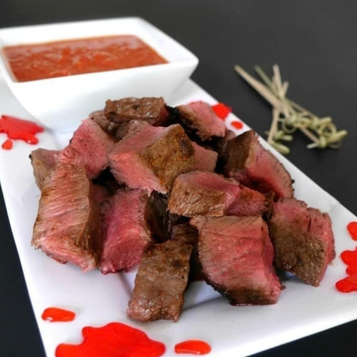 Halloween steak bites piled on a white platter with a bowl of roasted tomato garlic dip