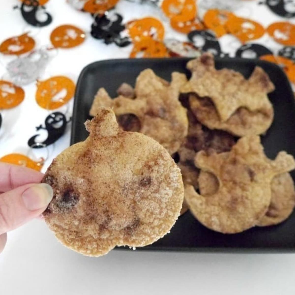 Halloween tortilla chips cut into pumpkin and ghost shapes on a black plate