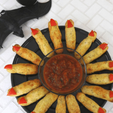 Low carb Halloween witch fingers with red bell pepper nails arranged around a bowl of salsa