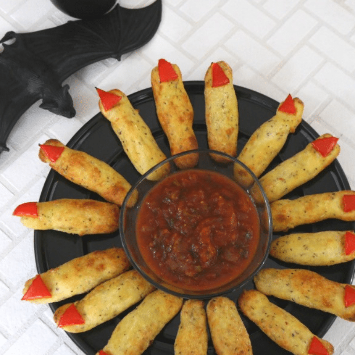 Low carb Halloween witch fingers with red bell pepper nails arranged around a bowl of salsa