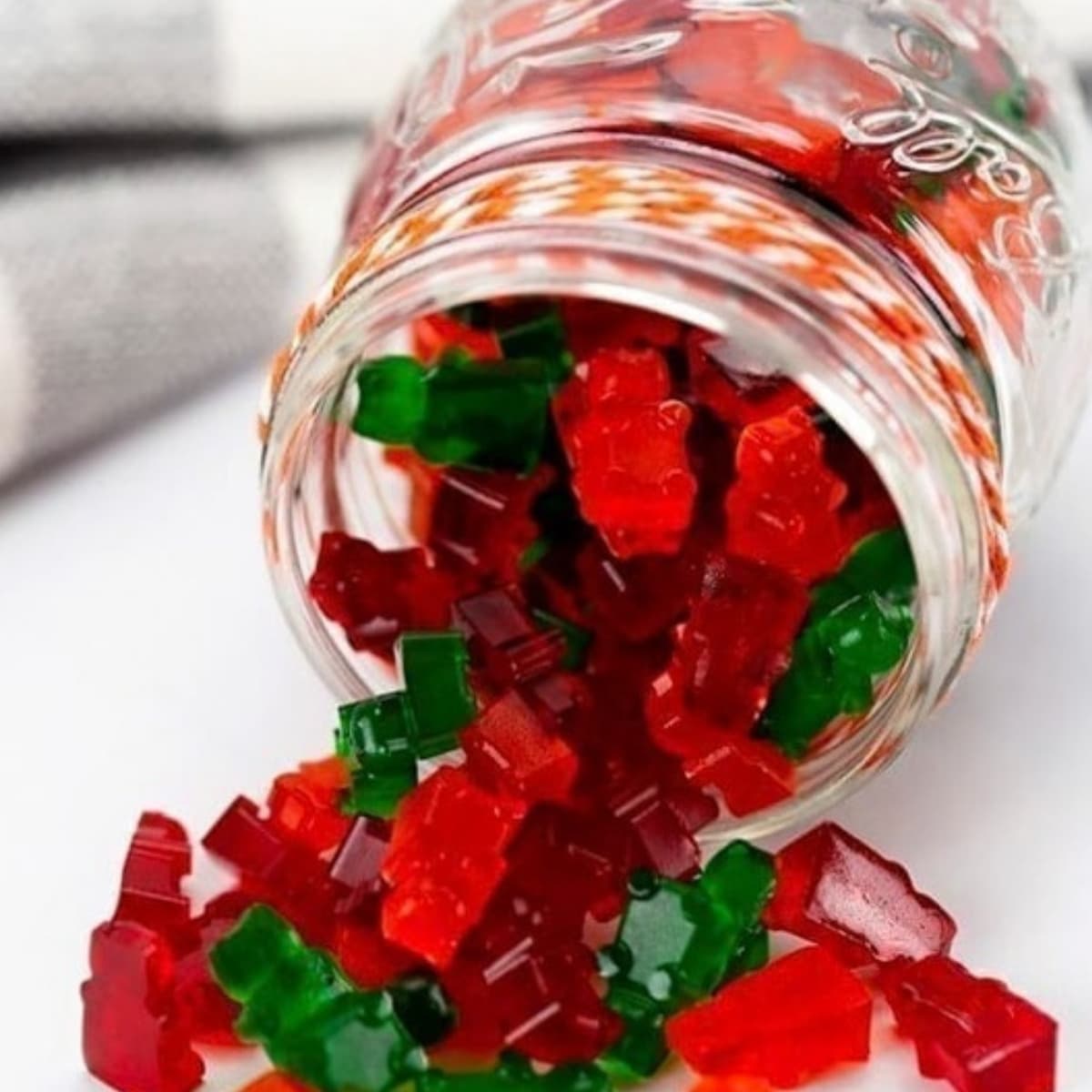 Red and green keto low carb gummy bears spilling out of a glass jar