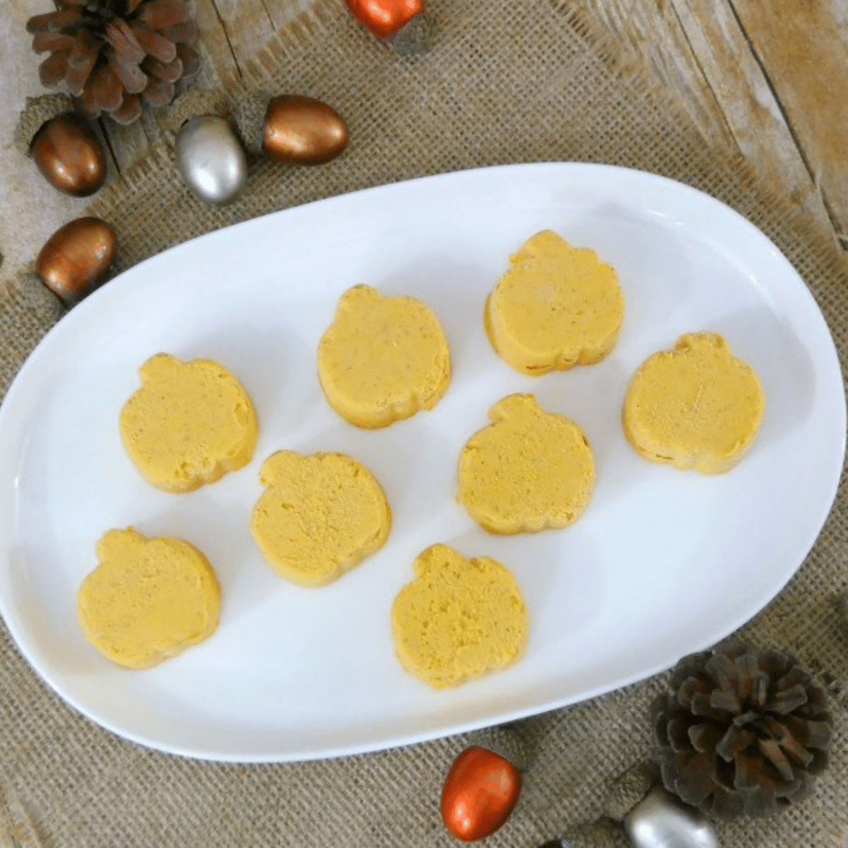 Pumpkin-shaped keto pumpkin fat bombs on a white oval plate with autumn acorns
