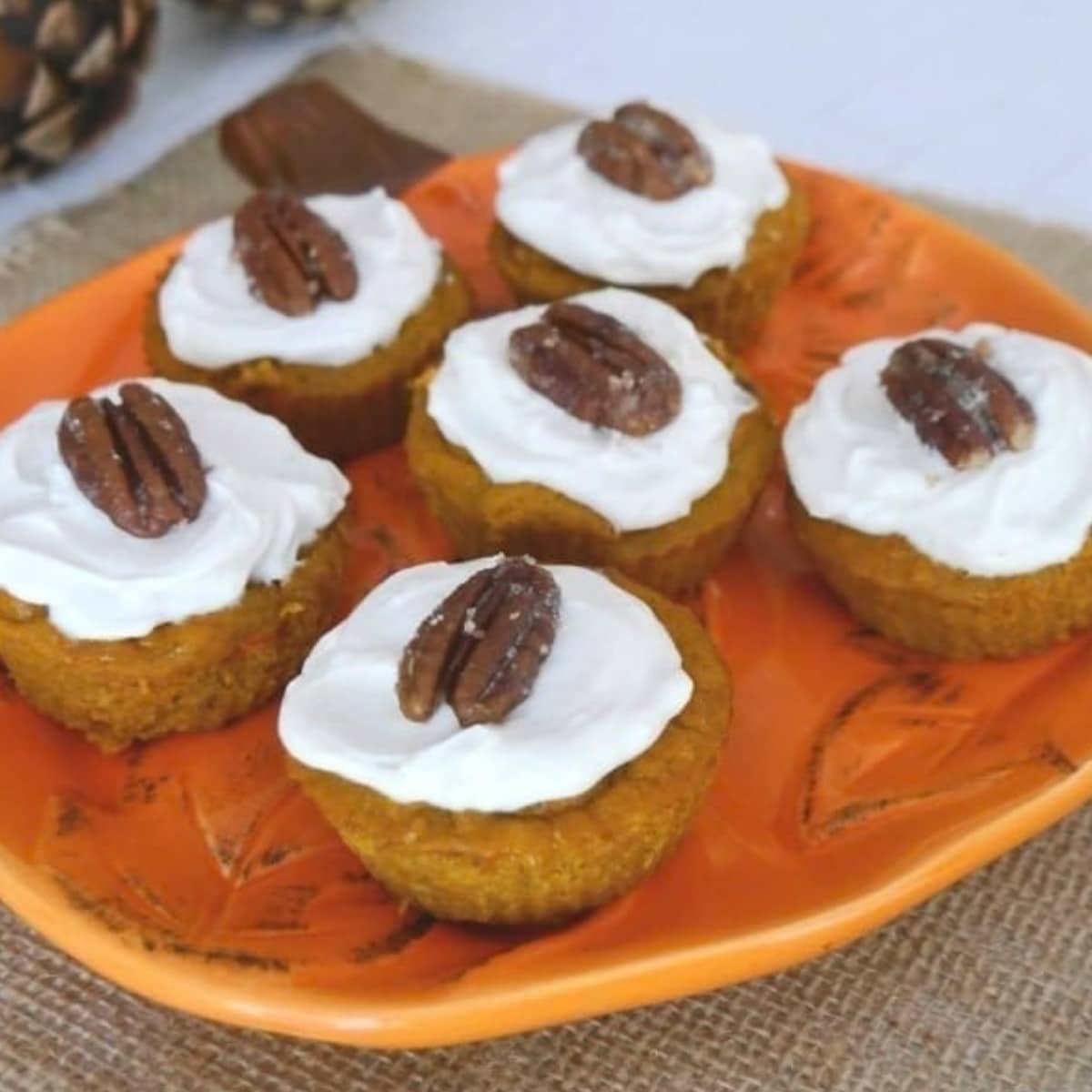 Keto pumpkin muffins with maple cream cheese frosting and caramelized pecans on an orange plate