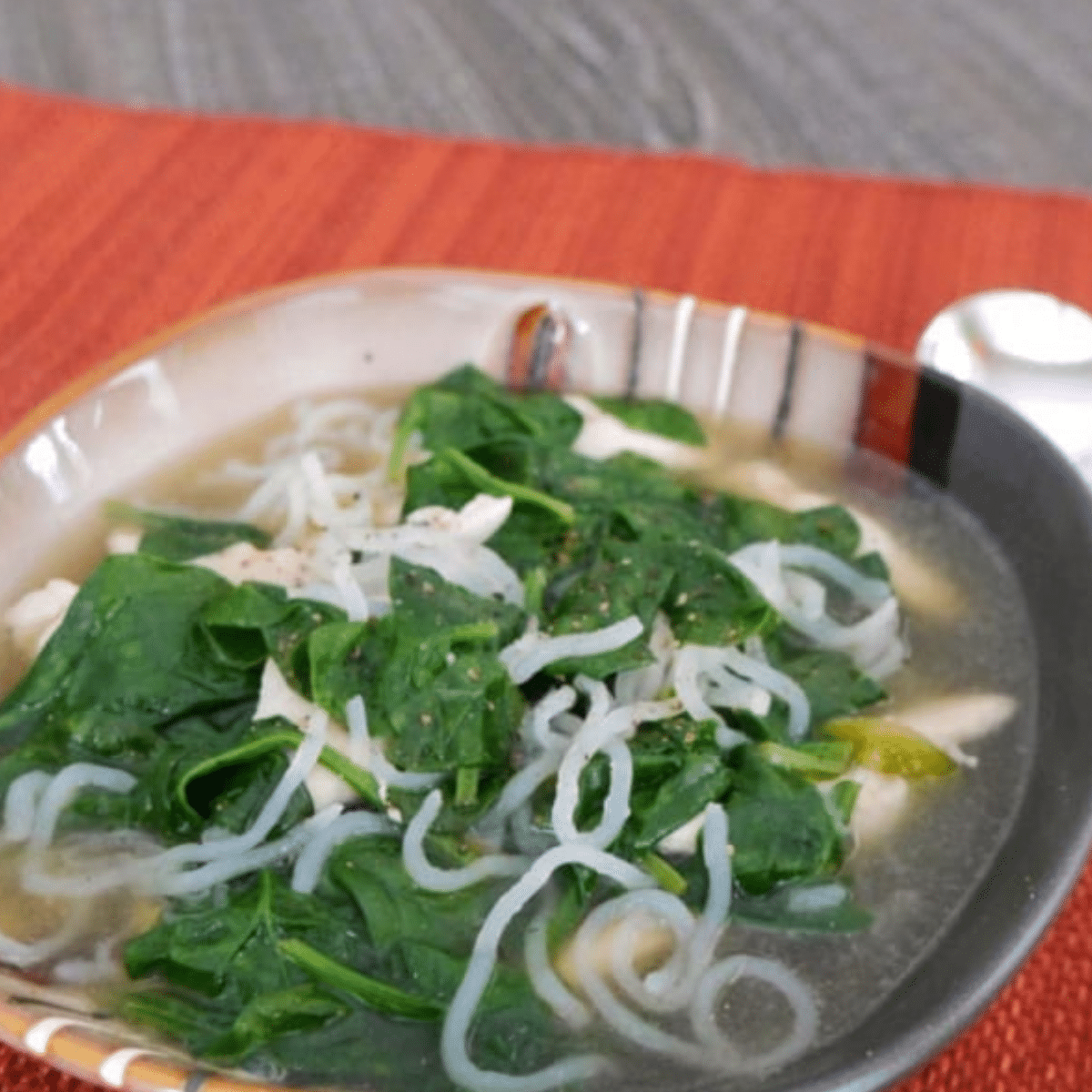 Bowl of low carb konjac noodle soup with chicken and baby spinach