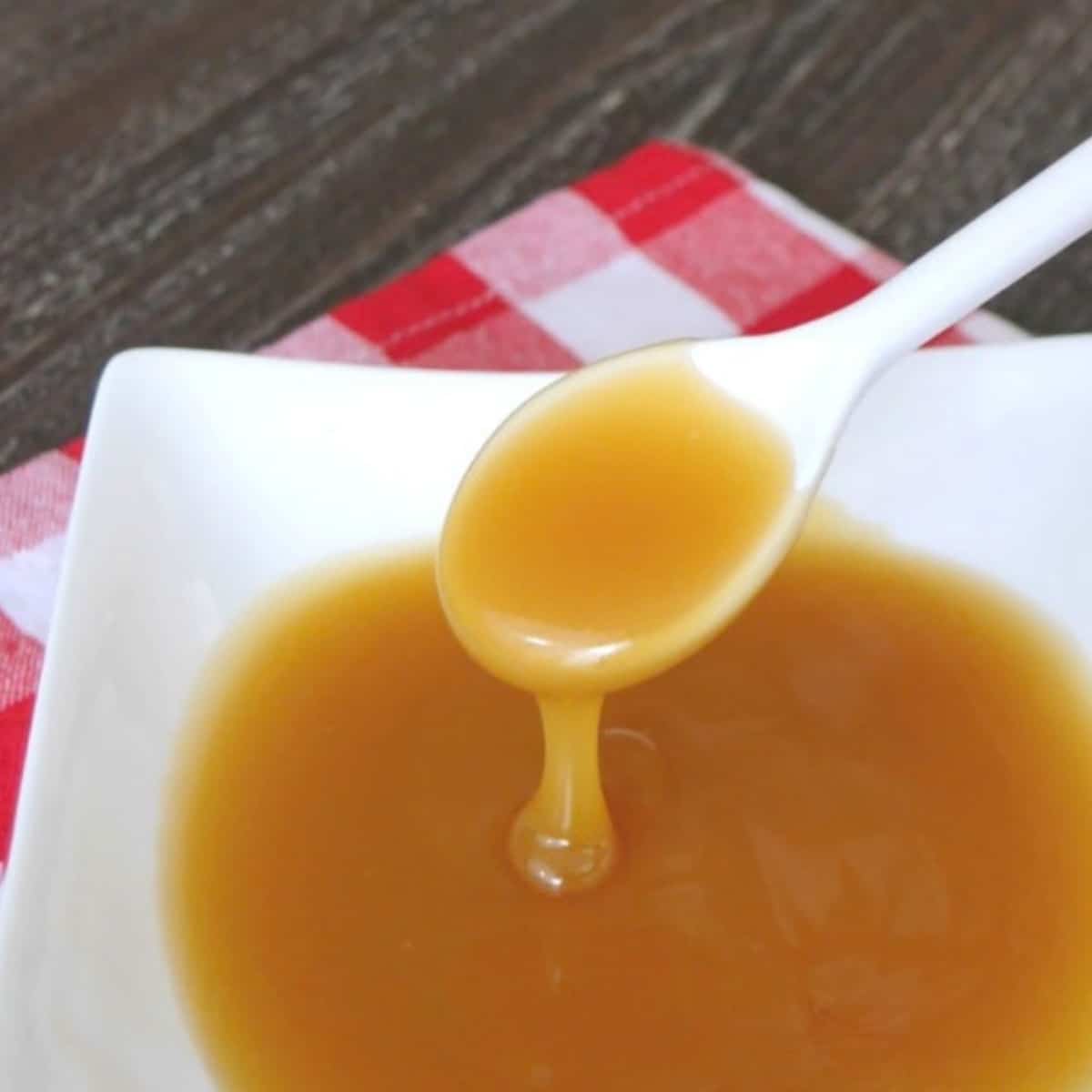 Low carb caramel sauce dripping from a white spoon into a bowl