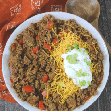 Low carb chili in a white bowl topped with shredded cheddar, sour cream and green onions