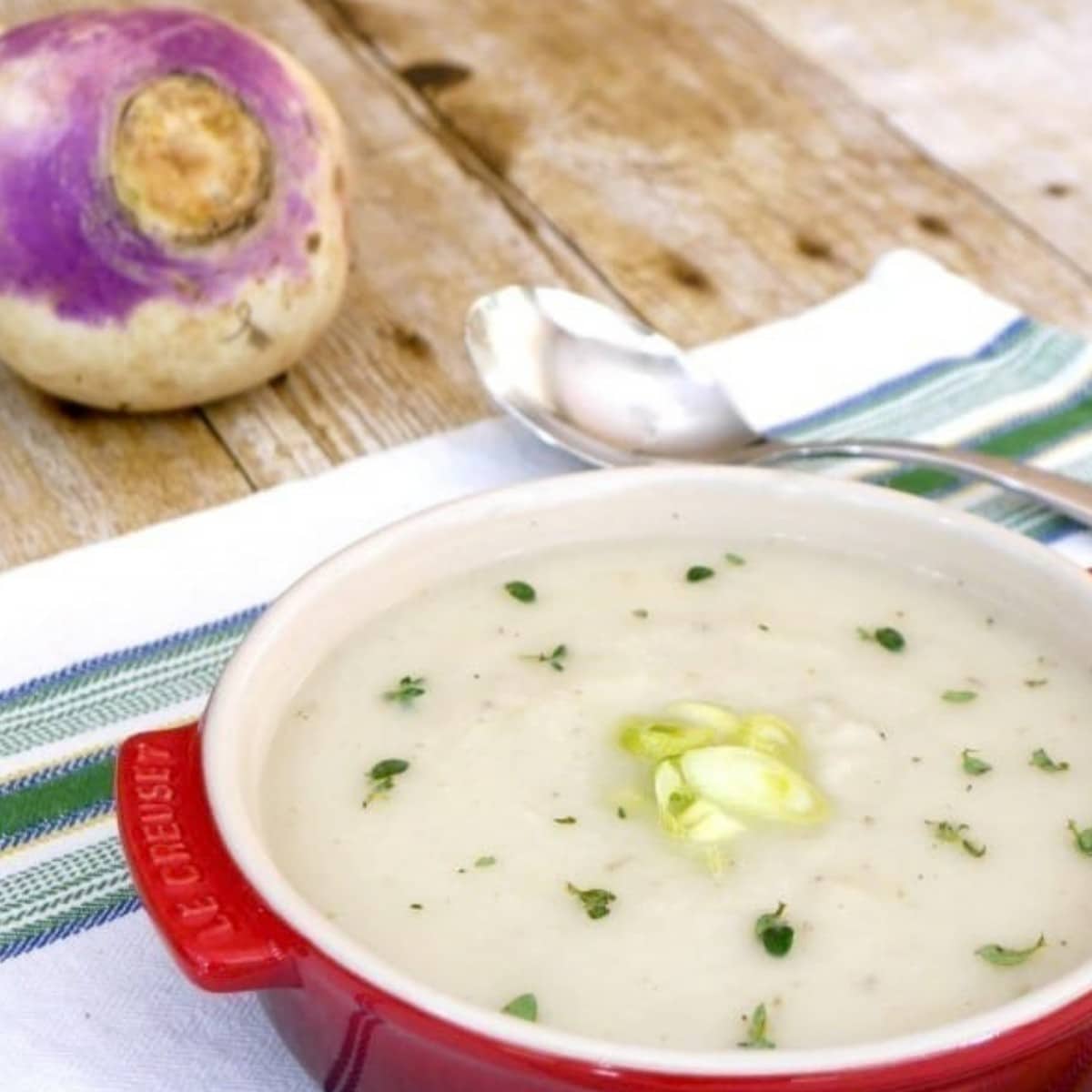 Low carb creamy turnip soup in a red bowl with a whole turnip and a spoon behind it