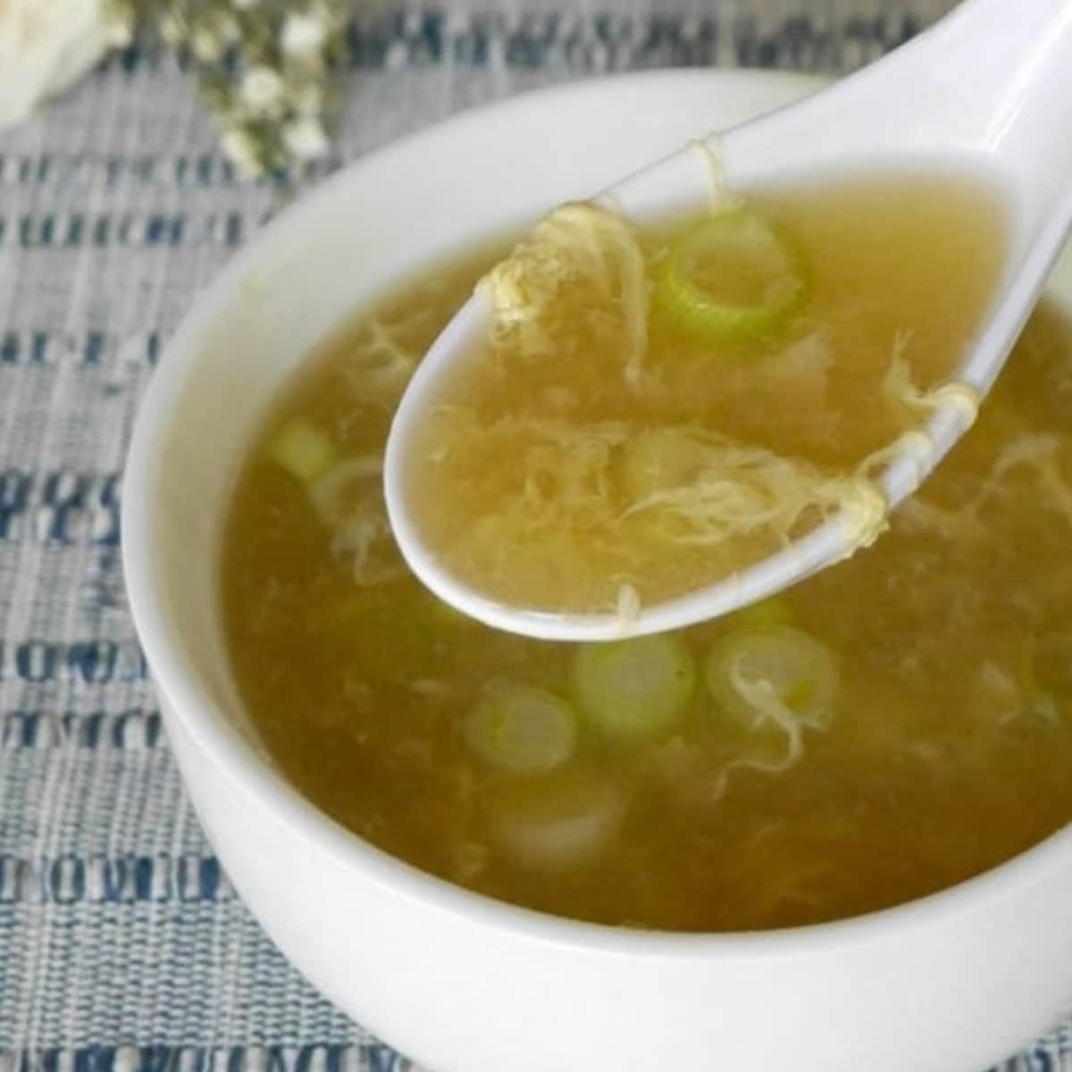Low carb egg drop soup in a white bowl with a spoonful of silky egg ribbons and green onions