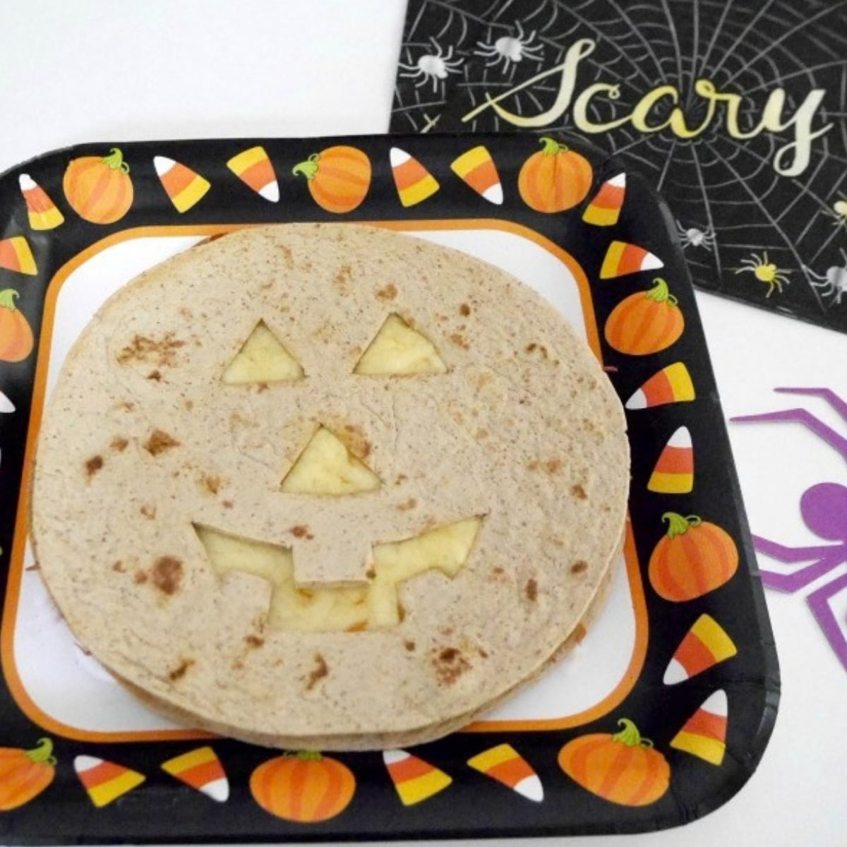 Low carb Halloween quesadilla with a cut-out jack-o'-lantern face on a Halloween paper plate