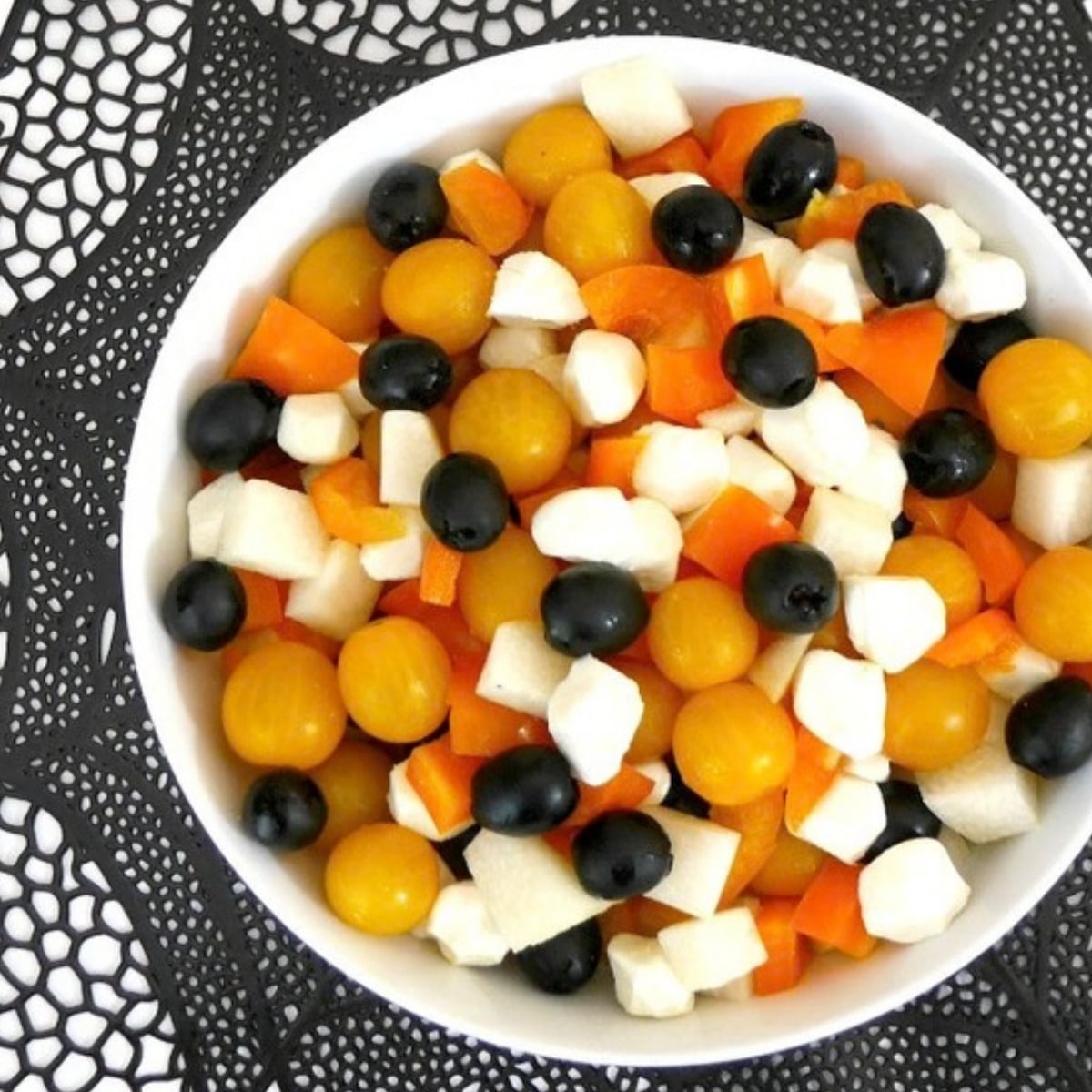 Low carb Halloween salad with orange bell pepper, golden cherry tomatoes, jicama, mozzarella pearls and black olives in a white bowl