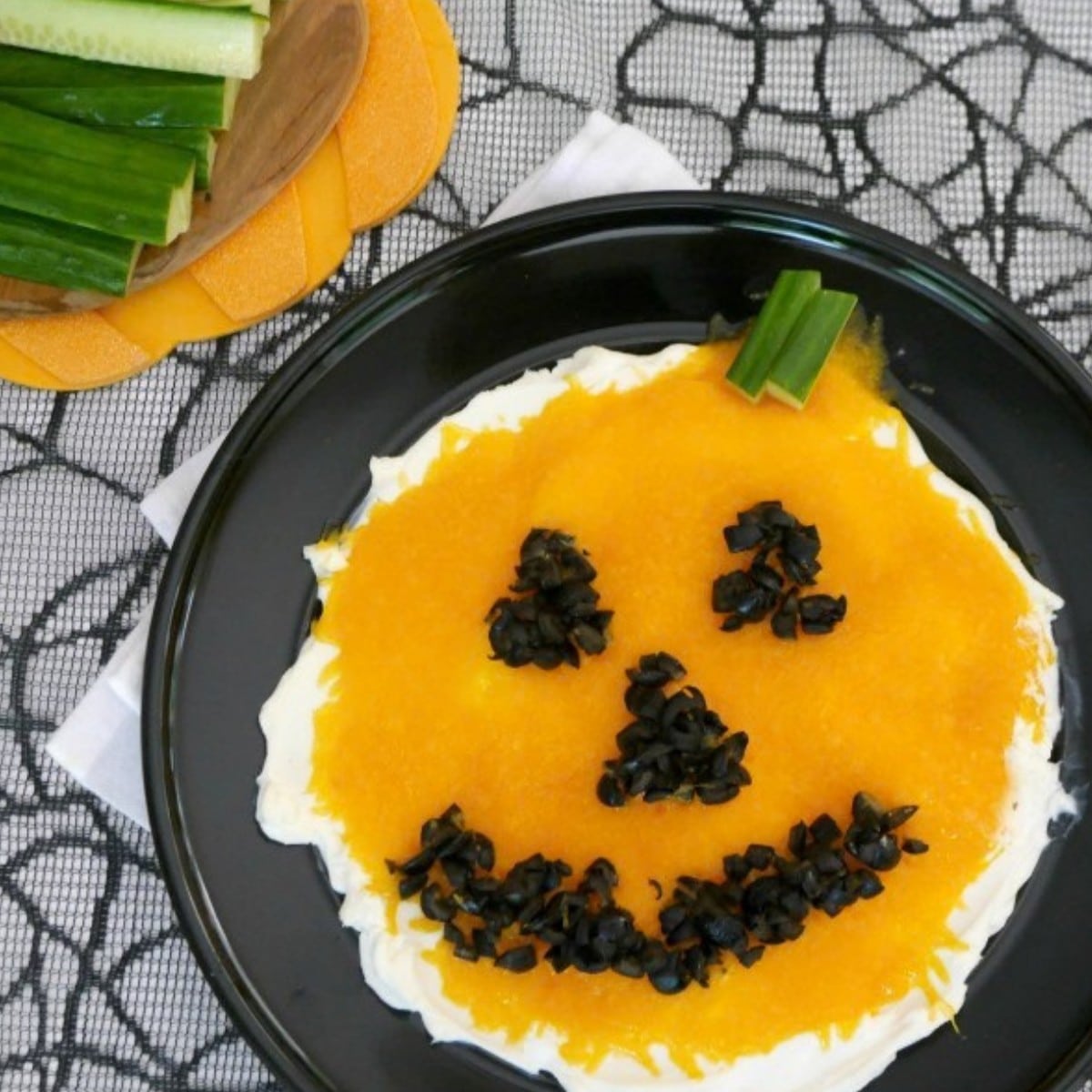 Low carb jack o'lantern dip made with cream cheese, melted cheddar and black olive face on a black plate