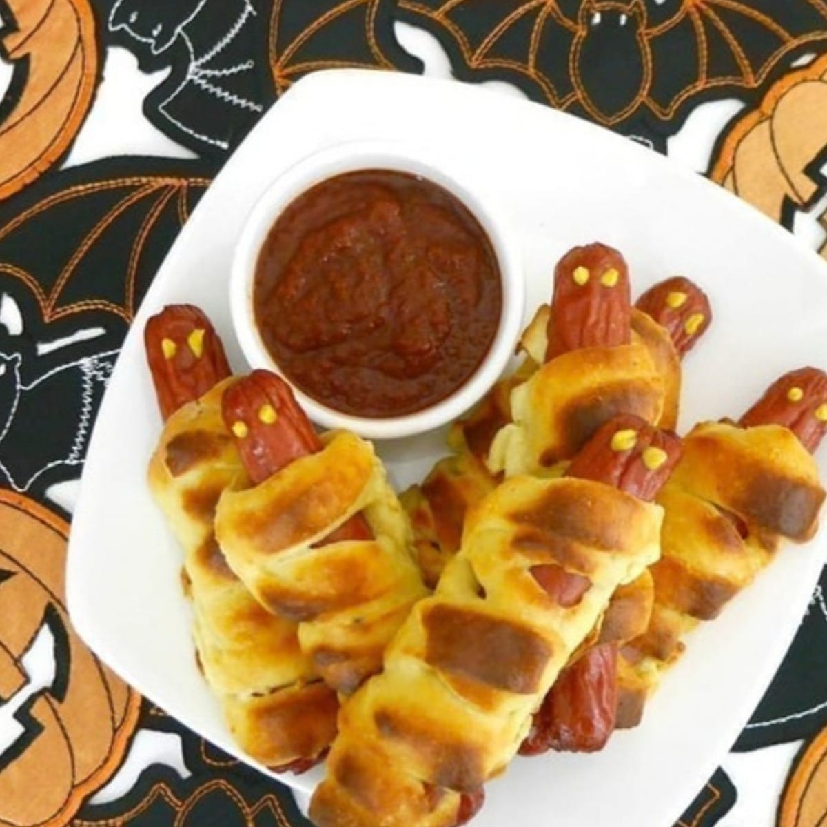 Low carb mummy hot dogs wrapped in fathead dough on a white plate with a bowl of ketchup