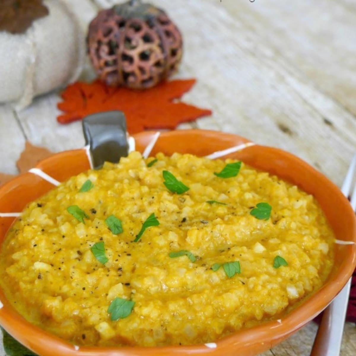 Low carb pumpkin cauliflower risotto in an orange bowl, garnished with parsley