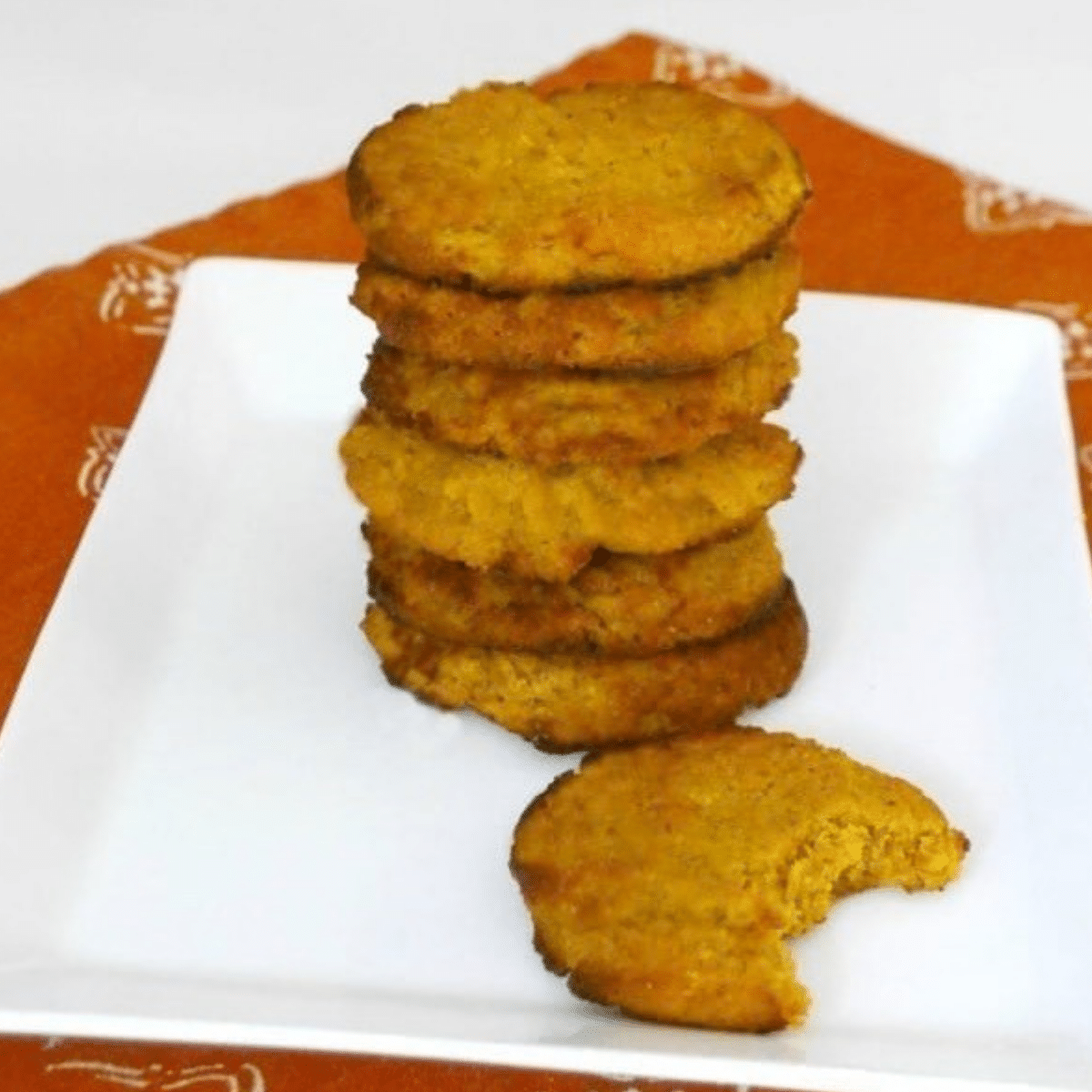 Stack of low carb pumpkin ricotta cookies on a white plate with one bitten cookie