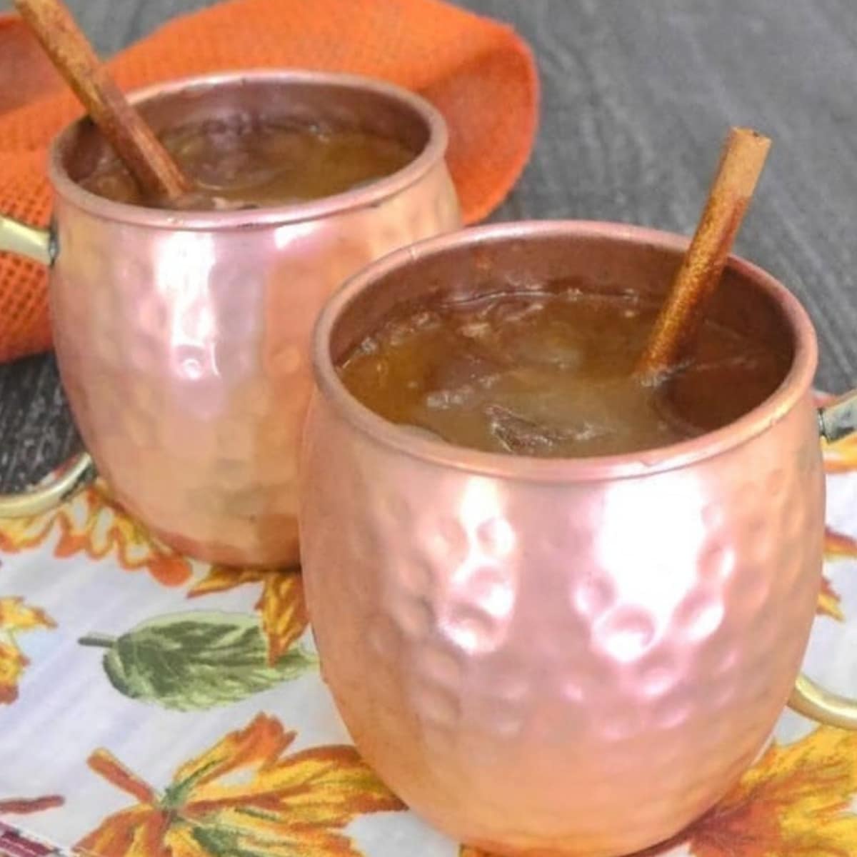 Two copper mugs of low carb pumpkin Moscow mule with cinnamon sticks