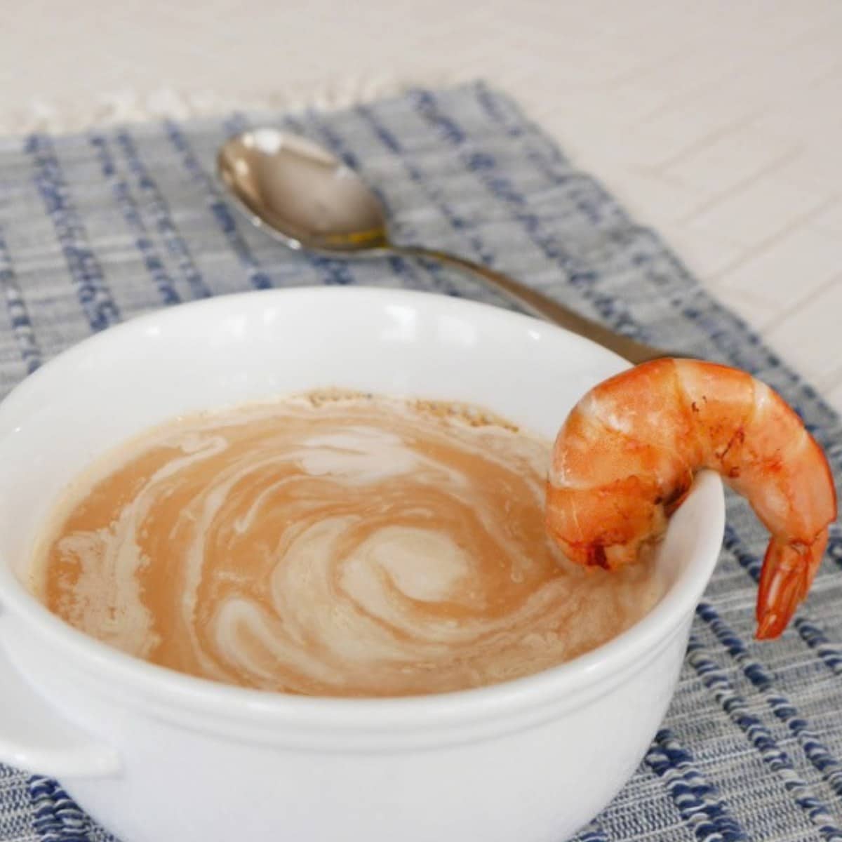 Low carb shrimp bisque in a white bowl with a swirl of cream and a pan-fried shrimp on the rim