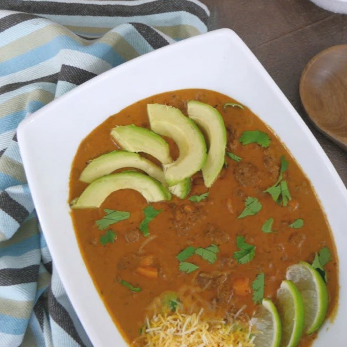 Bowl of low carb taco soup topped with avocado slices, cilantro, shredded cheese and lime wedges