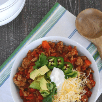 Low carb turkey chili in a white bowl topped with avocado, sour cream, cheese, cilantro and jalapeno