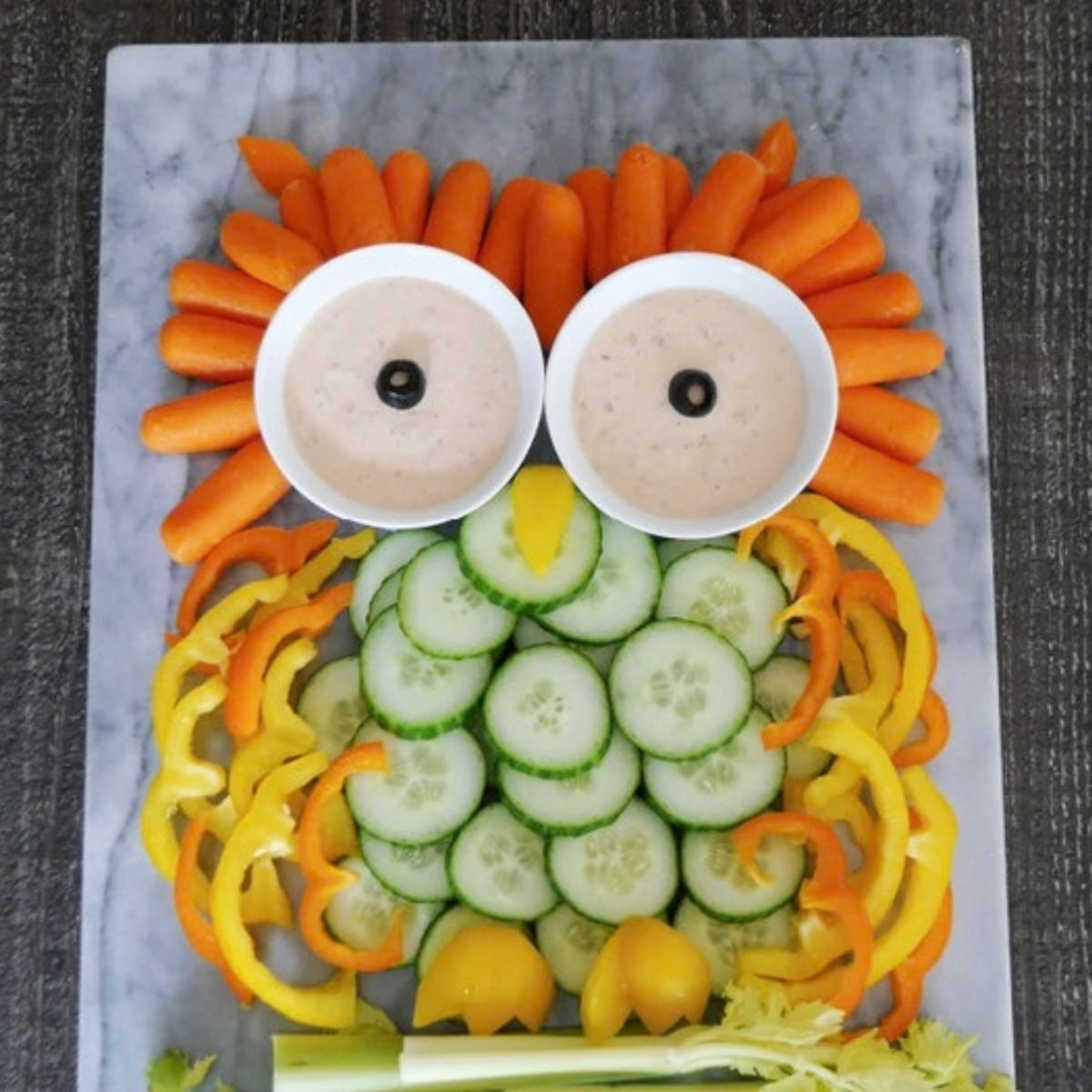 Owl veggie tray made from baby carrots, cucumber slices, bell peppers and celery with two bowls of chipotle ranch dip for eyes